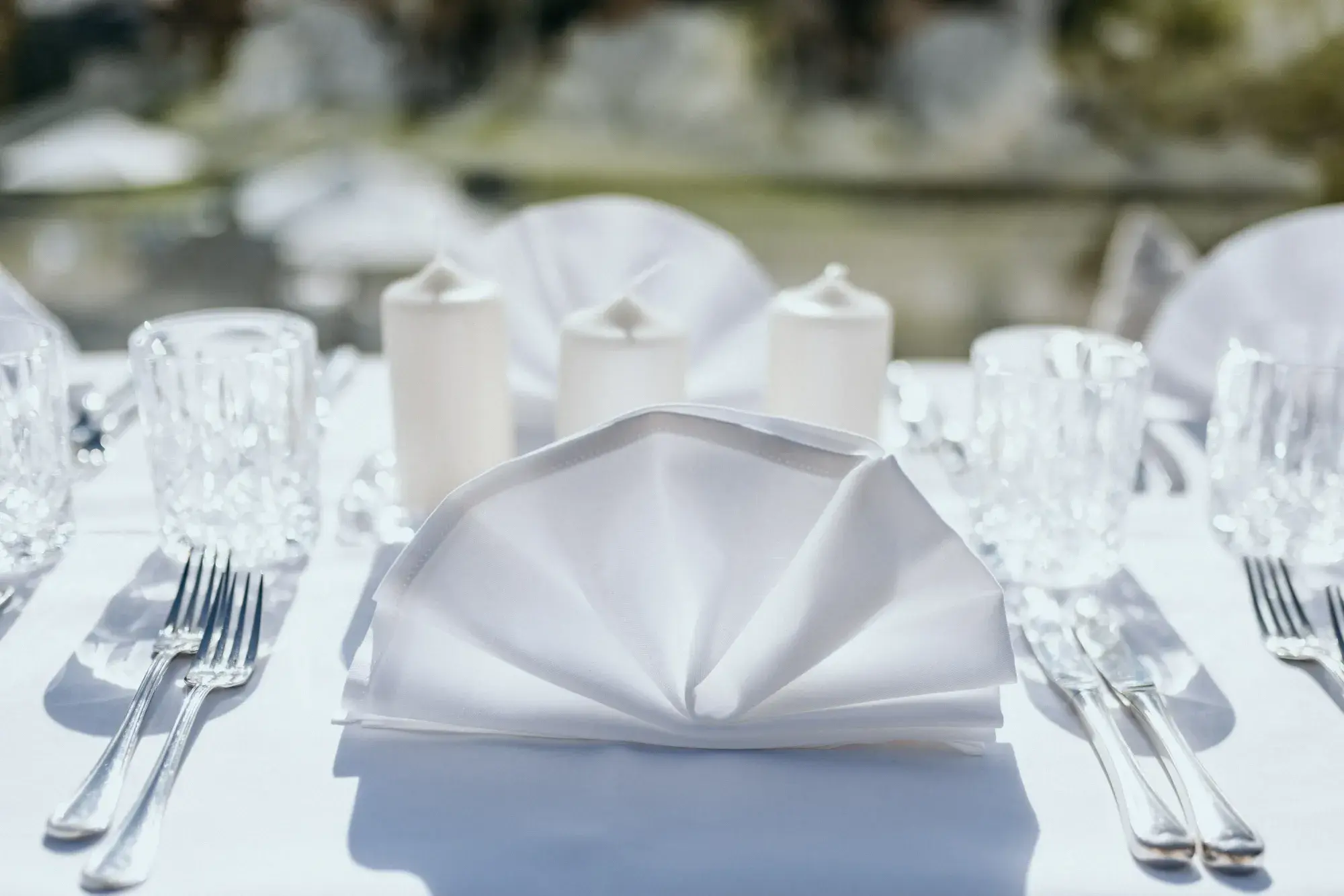 Fanned white napkin with candles and crystal glasses on a bright outdoor banquet table at the Stöttlalm in Tyrol
