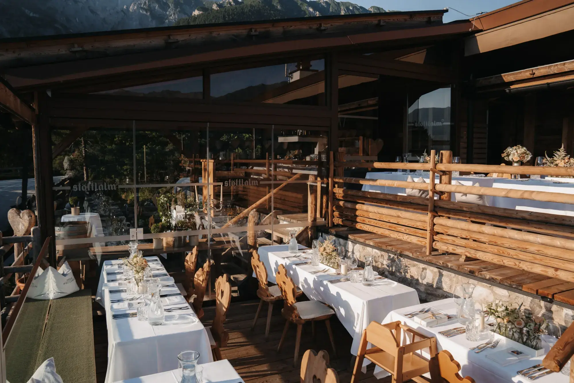 Long festive tables with Tyrolean wooden chairs on the terrace in evening light before the Mieminger Kette at the Stöttlalm