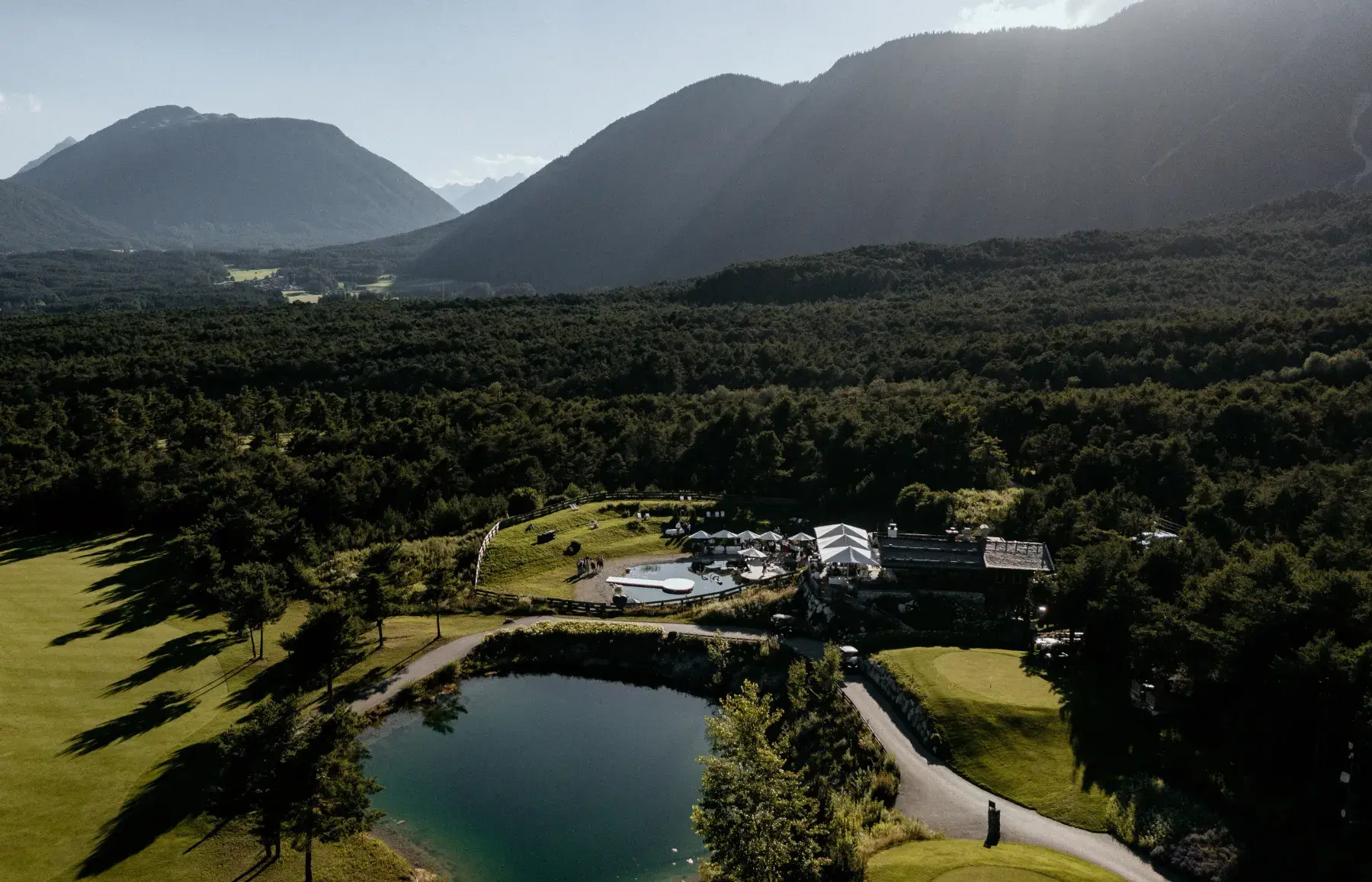 Aerial panorama of the Stöttlalm between golf course, mountain lake and forested slopes on the Mieming Plateau in Tyrol