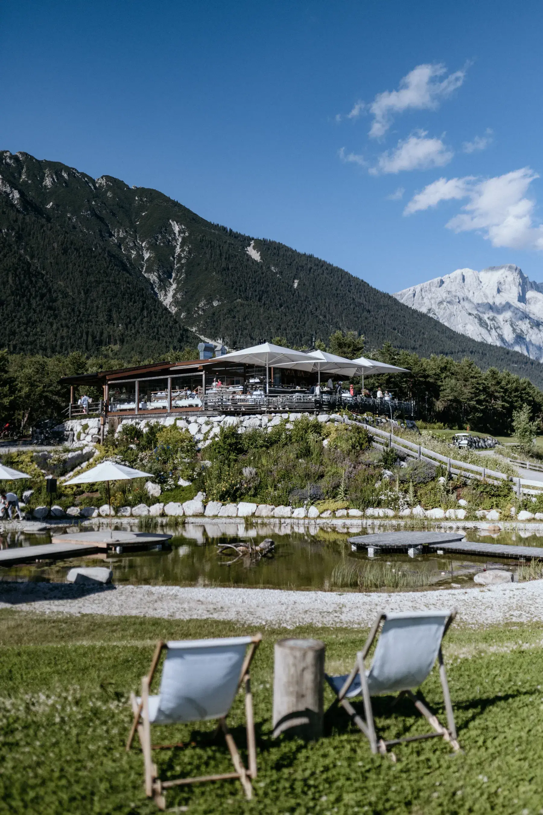 Stöttlalm mit überdachter Sonnenterrasse über dem Stöttlalmsee, Liegestühle auf der Wiese vor der Kulisse der Mieminger Kette