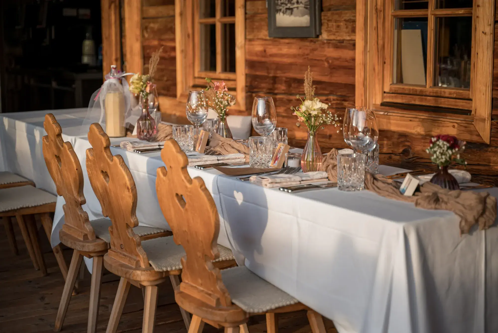Family celebration table with carved Tyrolean wooden chairs and flowers by the Stöttlalm alpine hut facade
