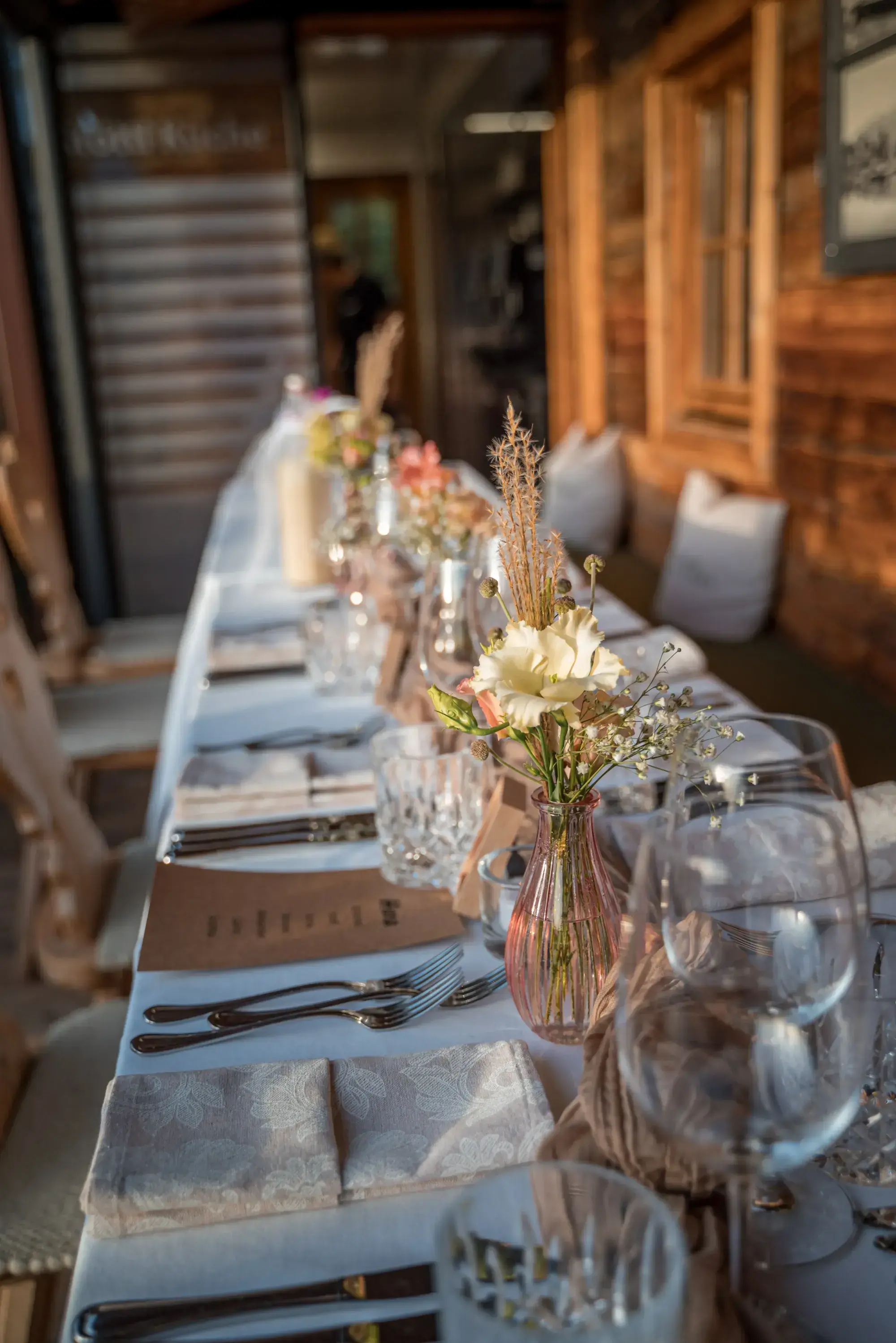 Long banquet table with dried flowers and crystal glasses on the terrace for a corporate event at the Stöttlalm in Tyrol