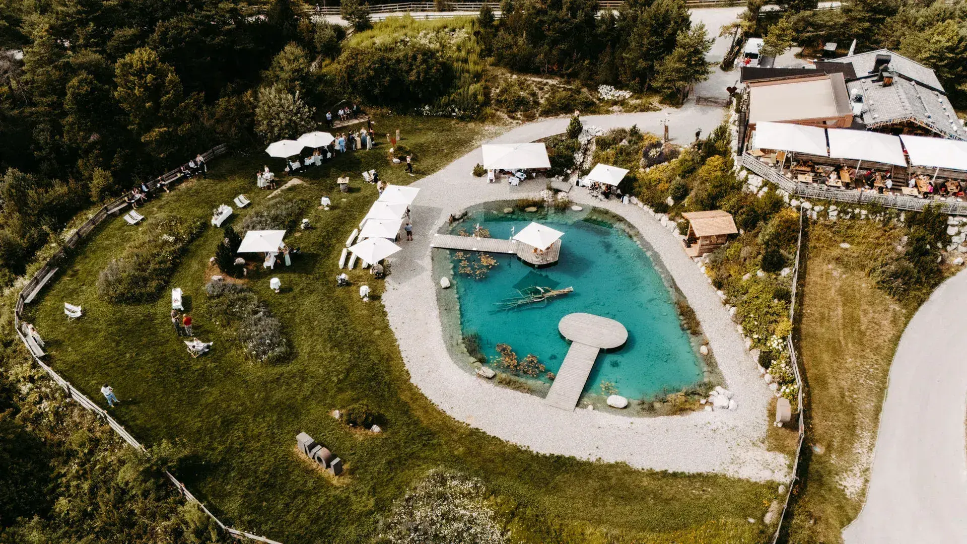 Aerial view of the turquoise Stöttlalmsee with jetty, pavilions and alpine hut amid meadows on the Mieminger Plateau, an event setting in Tyrol