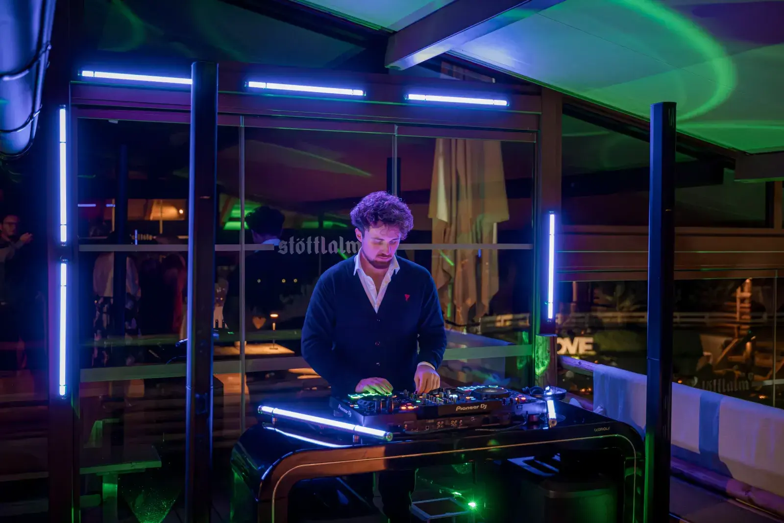 Partner DJ at a Pioneer console under blue and green party lights during a wedding on the glazed Stöttlalm terrace in Mieming, Tyrol