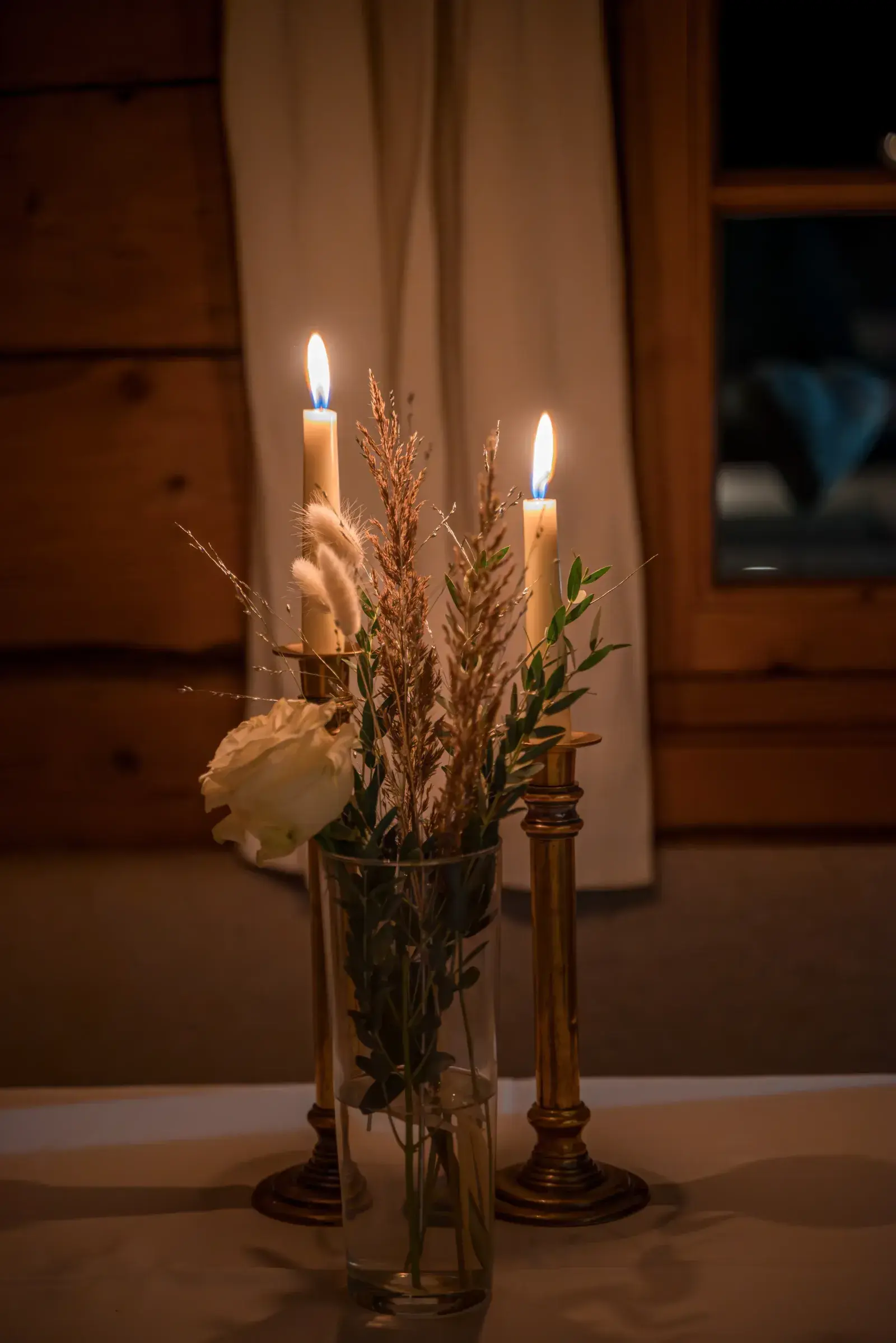 Candlelit table decoration with taper candles, a white rose and dried flowers in the cosy wood-panelled Stöttlalm Stube