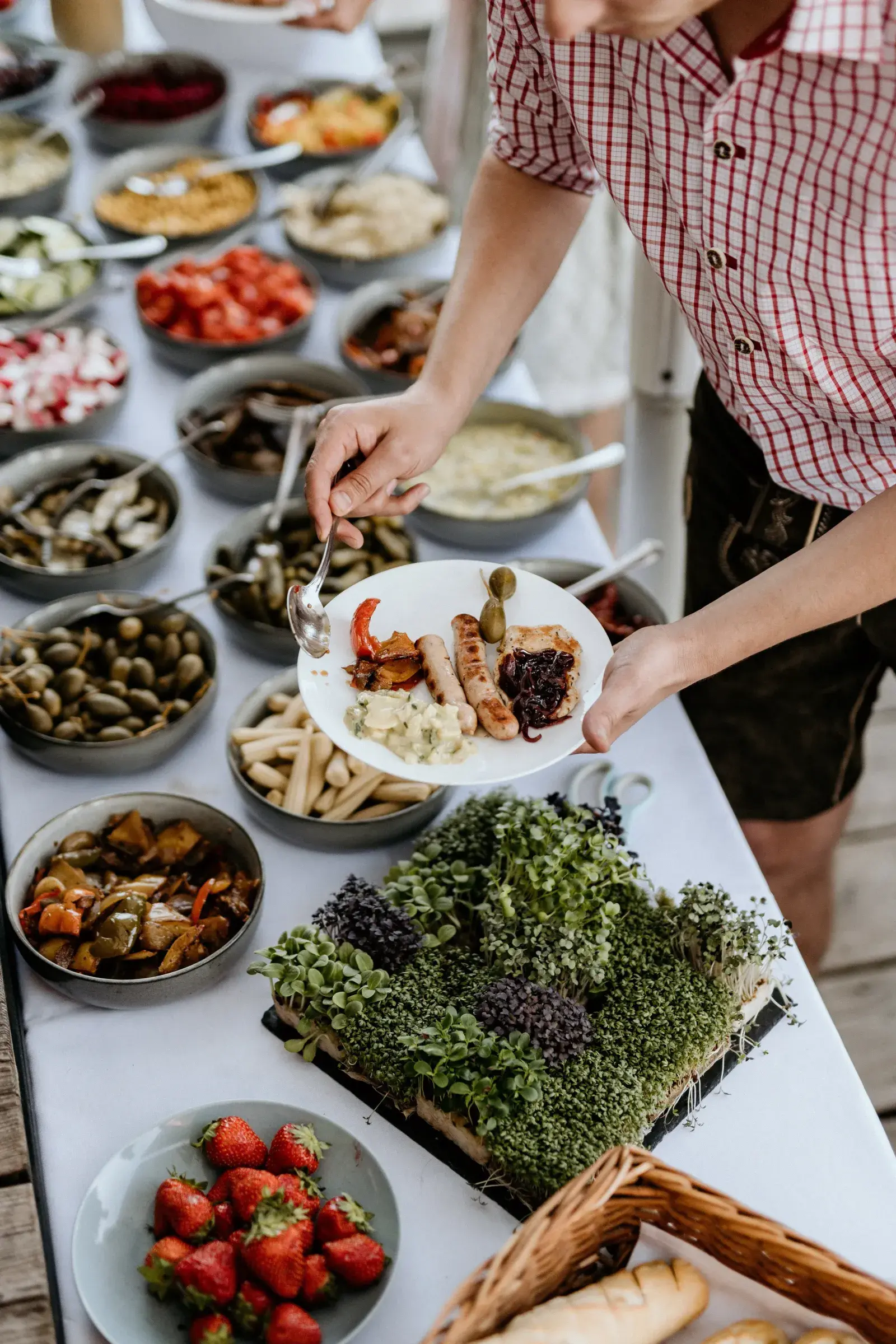 Guest in lederhosen filling a plate with sausage, antipasti and sides at the abundant Labestation buffet at the Stöttlalm